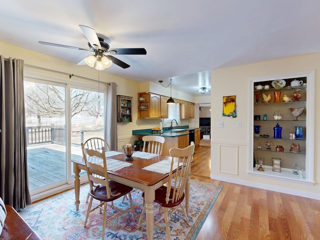 dining area featuring built in features, a wainscoted wall, ceiling fan, light wood-style floors, and a decorative wall