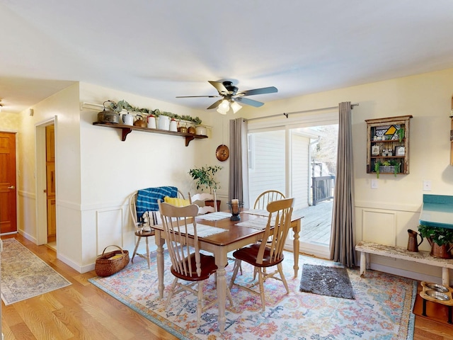 dining room featuring a decorative wall, a ceiling fan, light wood-type flooring, and wainscoting