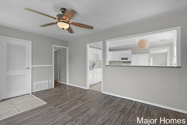 unfurnished living room featuring visible vents, a sink, wood finished floors, baseboards, and ceiling fan