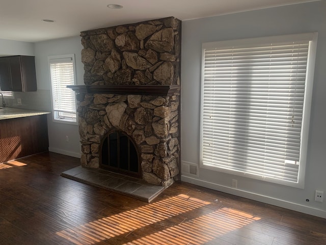 unfurnished living room featuring visible vents, baseboards, a stone fireplace, hardwood / wood-style flooring, and a sink