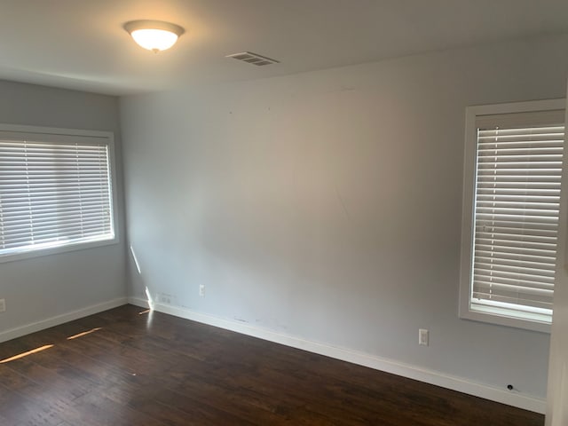 empty room featuring visible vents, dark wood-type flooring, and baseboards