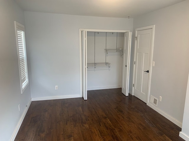 unfurnished bedroom with dark wood-style floors, visible vents, a closet, and baseboards