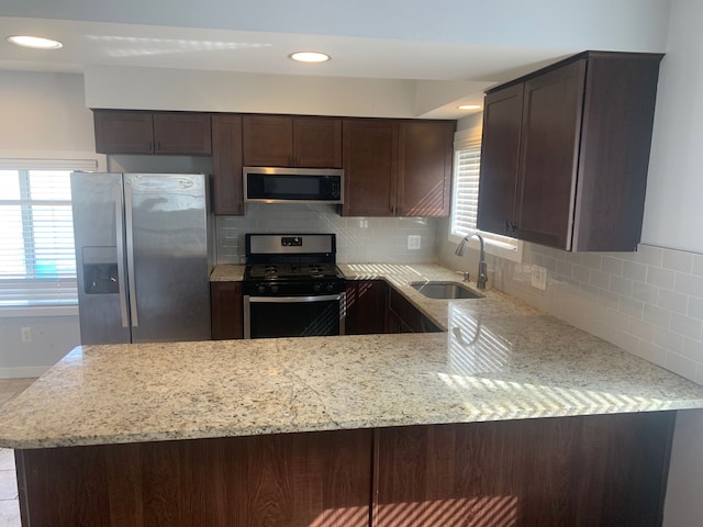 kitchen featuring dark brown cabinetry, light stone countertops, appliances with stainless steel finishes, and a sink