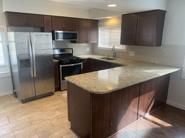 kitchen with a sink, dark brown cabinetry, appliances with stainless steel finishes, and a peninsula