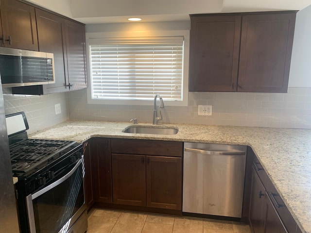 kitchen with a sink, light stone counters, backsplash, stainless steel appliances, and dark brown cabinets