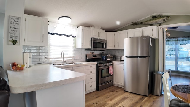 kitchen with a sink, stainless steel appliances, vaulted ceiling, light countertops, and white cabinetry