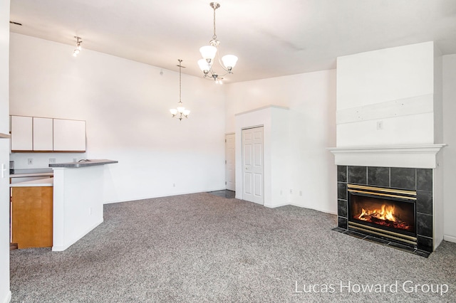 unfurnished living room with high vaulted ceiling, a notable chandelier, carpet, and a tile fireplace