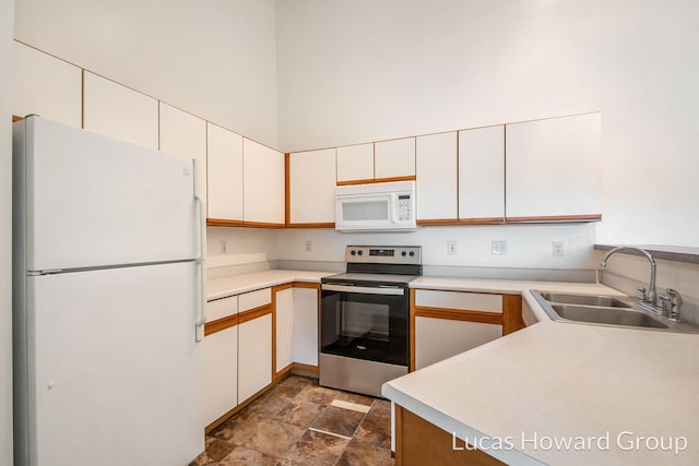 kitchen featuring white appliances, light countertops, a towering ceiling, and a sink