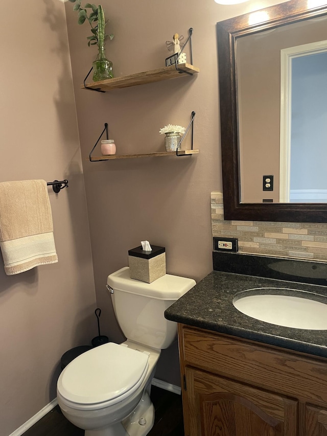 half bath featuring vanity, toilet, baseboards, and backsplash