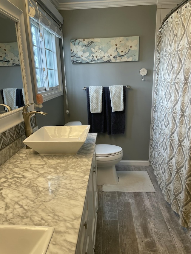 bathroom with vanity, wood finished floors, baseboards, crown molding, and toilet