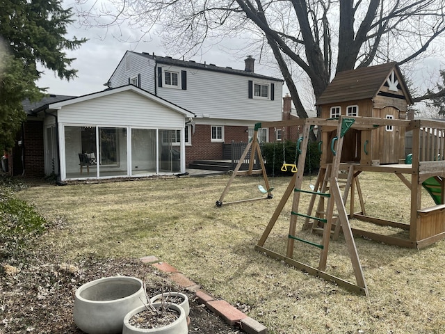 rear view of house with brick siding, a chimney, a playground, and a sunroom