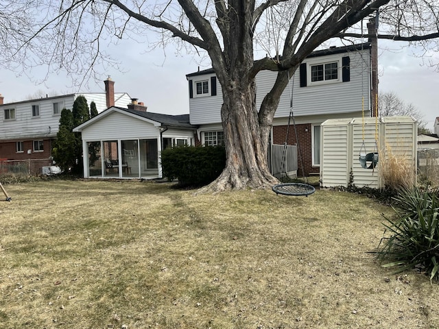 rear view of house with brick siding, fence, a yard, and a sunroom