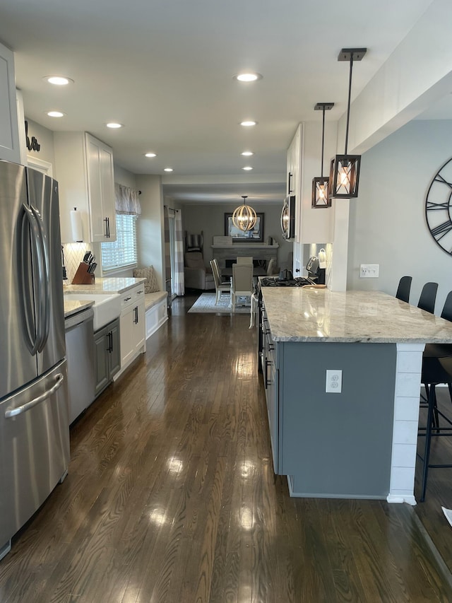 kitchen featuring white cabinetry, appliances with stainless steel finishes, a breakfast bar area, light stone countertops, and dark wood-style flooring