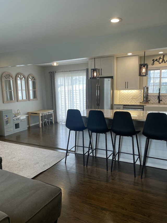 kitchen with tasteful backsplash, dark wood-type flooring, light stone countertops, appliances with stainless steel finishes, and a kitchen breakfast bar