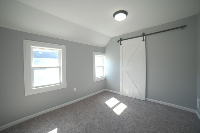 unfurnished bedroom with a barn door, carpet, baseboards, and vaulted ceiling