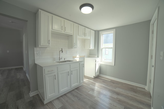 kitchen featuring a sink, tasteful backsplash, white cabinets, light wood finished floors, and baseboards