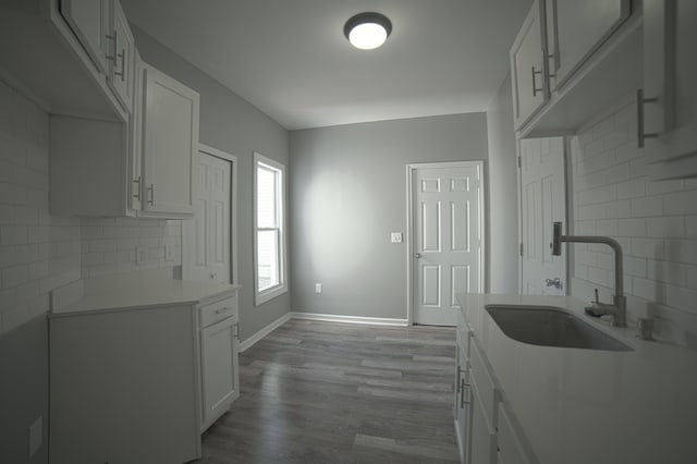 kitchen featuring baseboards, wood finished floors, tasteful backsplash, and a sink