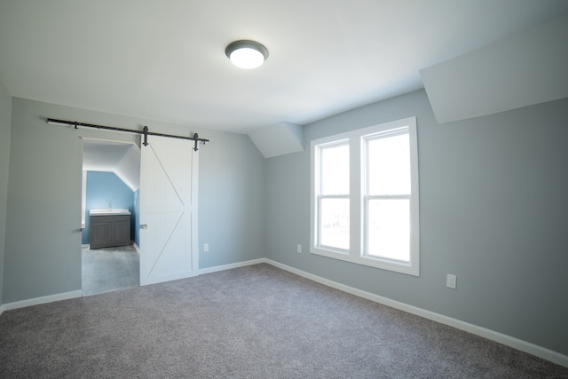 additional living space with carpet flooring, baseboards, lofted ceiling, and a barn door