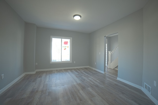 empty room featuring visible vents, baseboards, wood finished floors, and stairs