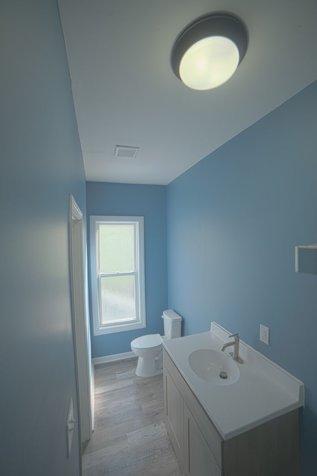 bathroom featuring visible vents, baseboards, toilet, wood finished floors, and vanity