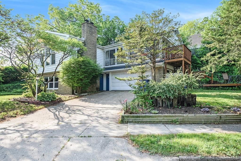 view of front of home featuring a balcony, a chimney, driveway, and an attached garage
