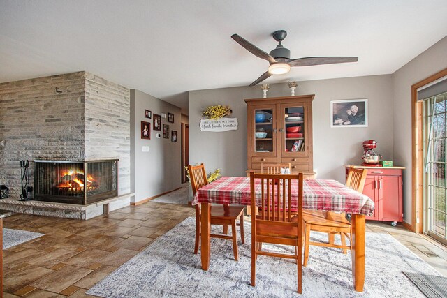 dining area featuring a stone fireplace, stone finish floor, baseboards, and ceiling fan