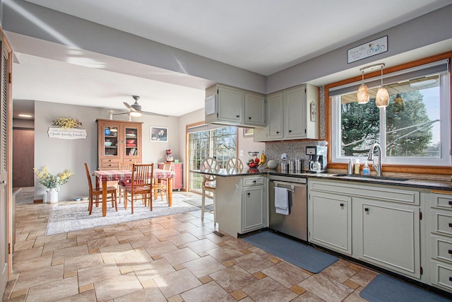 kitchen featuring dark countertops, stone finish flooring, dishwasher, a ceiling fan, and a sink