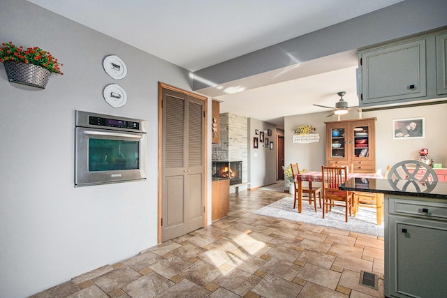 kitchen featuring visible vents, a ceiling fan, stone finish flooring, a large fireplace, and stainless steel oven