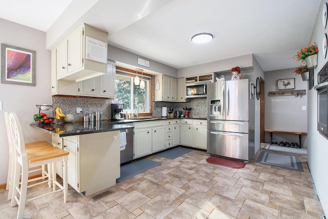 kitchen featuring a sink, backsplash, dark countertops, appliances with stainless steel finishes, and a peninsula