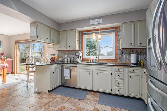 kitchen with a sink, stainless steel appliances, dark countertops, and a peninsula