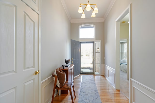 foyer with light wood-type flooring, a wainscoted wall, a notable chandelier, ornamental molding, and a decorative wall