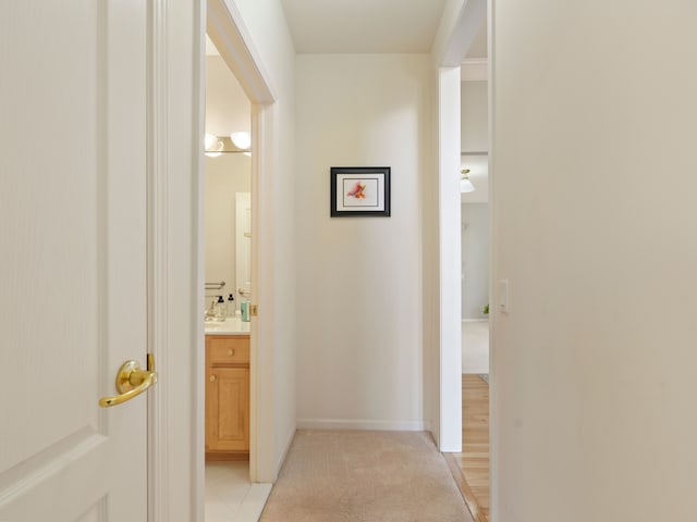 hall with a sink, baseboards, and light colored carpet