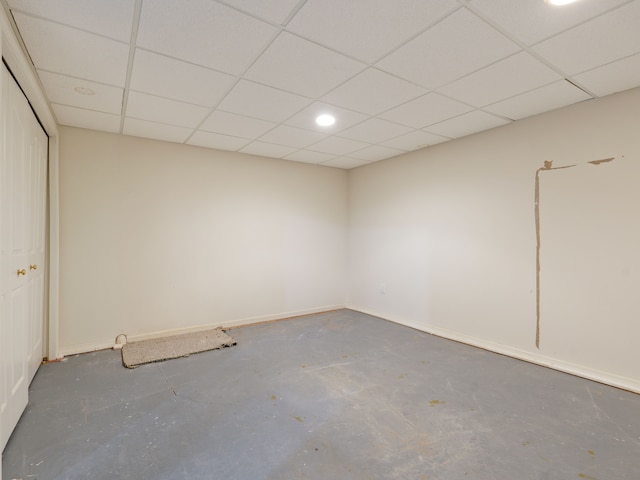 empty room with a paneled ceiling, baseboards, and concrete floors