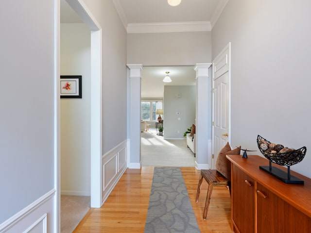 hallway featuring light wood finished floors, crown molding, and ornate columns