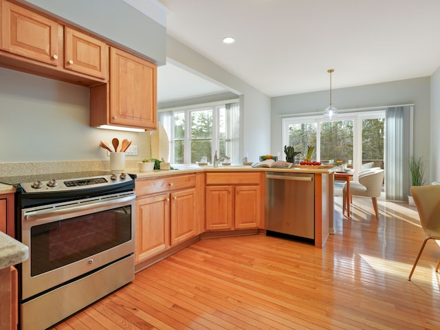 kitchen with light wood finished floors, light countertops, appliances with stainless steel finishes, hanging light fixtures, and a sink