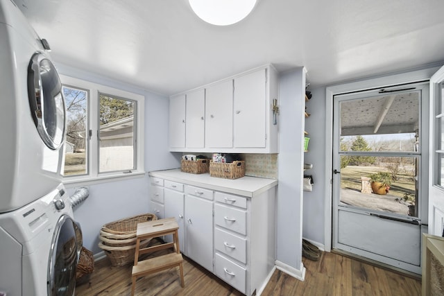 clothes washing area featuring cabinet space, wood finished floors, baseboards, and stacked washer and dryer