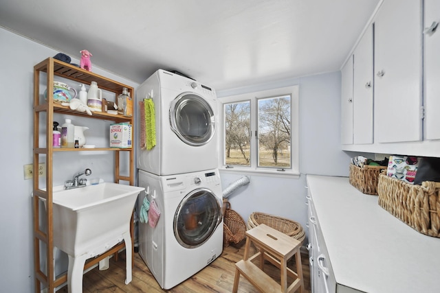 clothes washing area with stacked washing maching and dryer, light wood-type flooring, and cabinet space