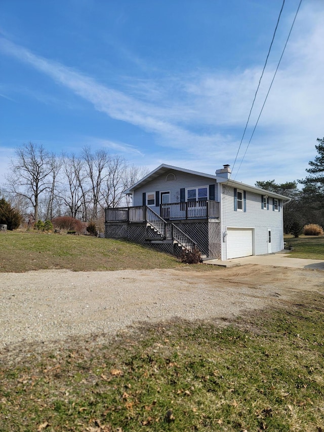 view of side of property with dirt driveway, a yard, an attached garage, a wooden deck, and a chimney