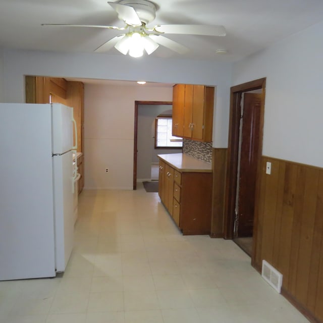 kitchen featuring wooden walls, visible vents, ceiling fan, brown cabinets, and freestanding refrigerator