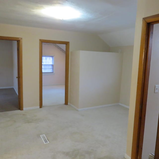 unfurnished room featuring visible vents, lofted ceiling, and light carpet