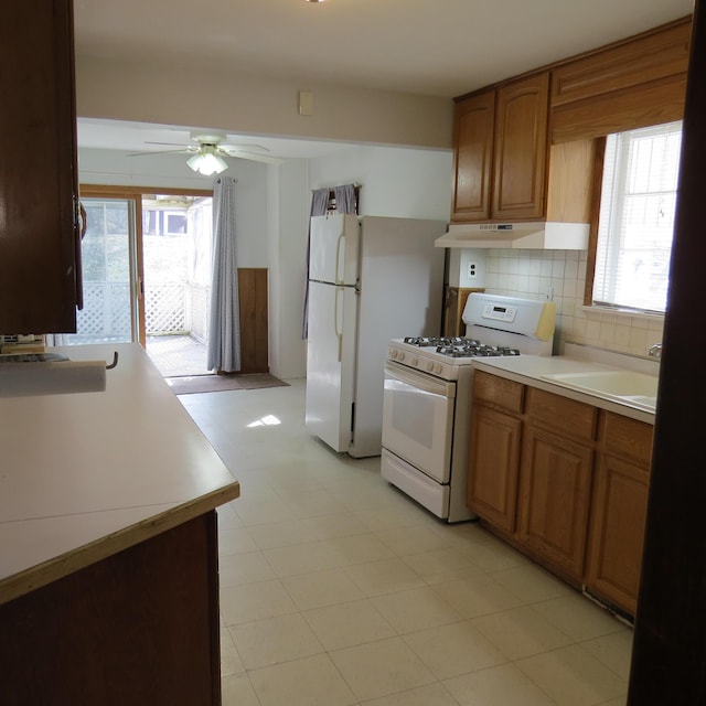 kitchen with a ceiling fan, white gas stove, a sink, under cabinet range hood, and backsplash