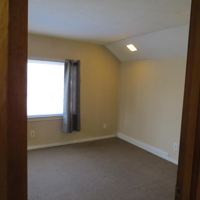 carpeted empty room with baseboards and vaulted ceiling