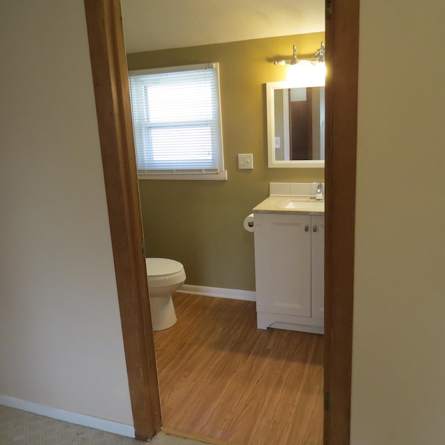 bathroom featuring baseboards, toilet, wood finished floors, and vanity