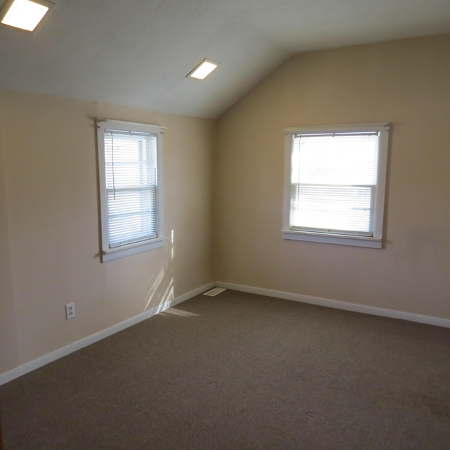 unfurnished room featuring dark colored carpet, baseboards, and vaulted ceiling