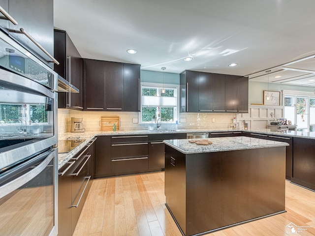 kitchen with a healthy amount of sunlight, stainless steel appliances, light wood-style flooring, and light stone countertops