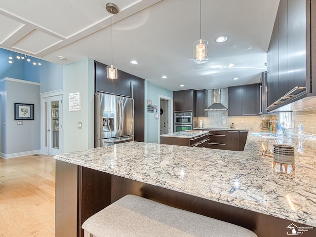 kitchen featuring wall chimney exhaust hood, light stone countertops, tasteful backsplash, and appliances with stainless steel finishes