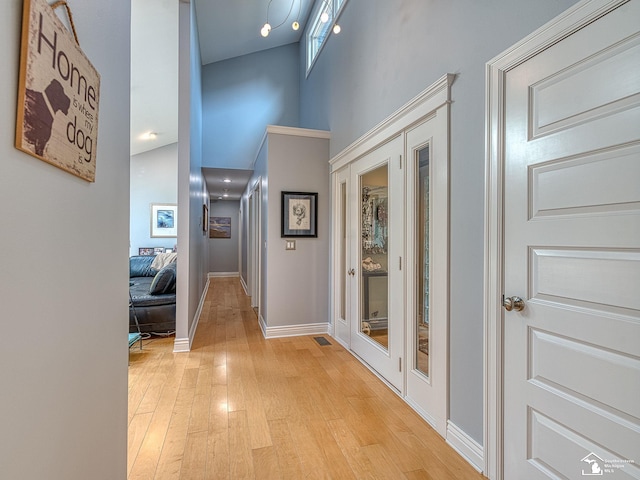 hall with light wood-style flooring, baseboards, and a high ceiling