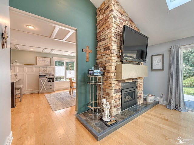 unfurnished living room featuring vaulted ceiling with skylight, plenty of natural light, wood finished floors, and a fireplace