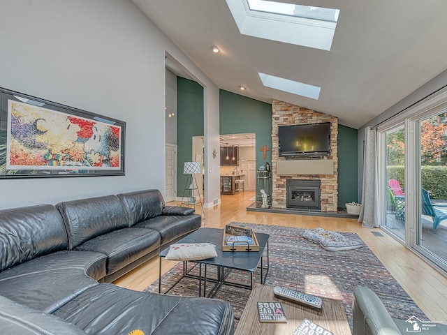 living area with wood finished floors, high vaulted ceiling, a stone fireplace, and a skylight