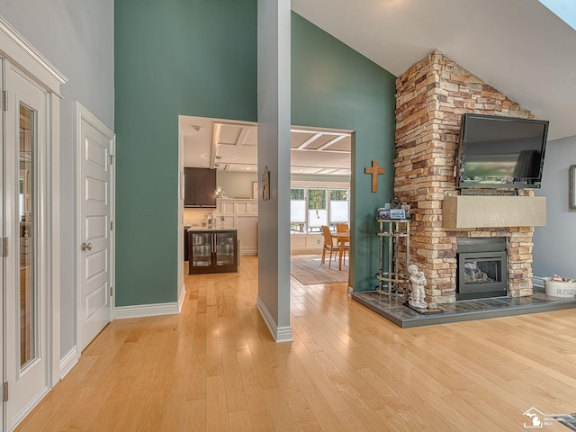 unfurnished living room featuring a stone fireplace, wood finished floors, baseboards, and high vaulted ceiling